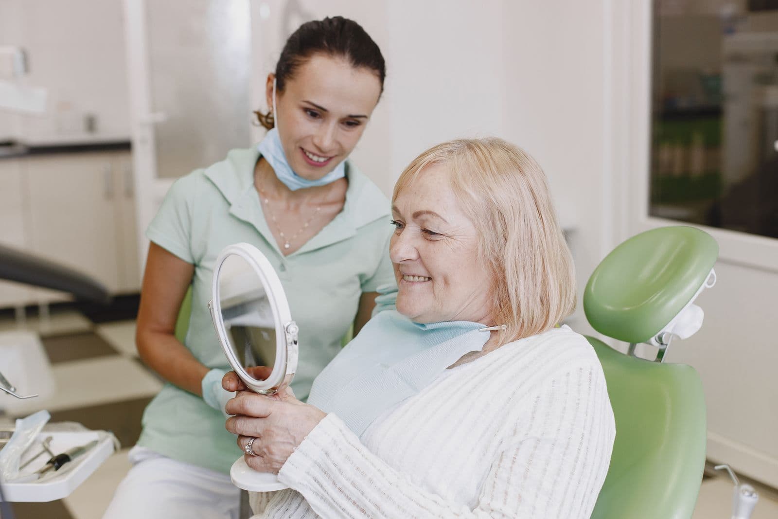 Patiente assise dans un fauteuil dentaire tenant un miroir, une dentiste à ses côtés